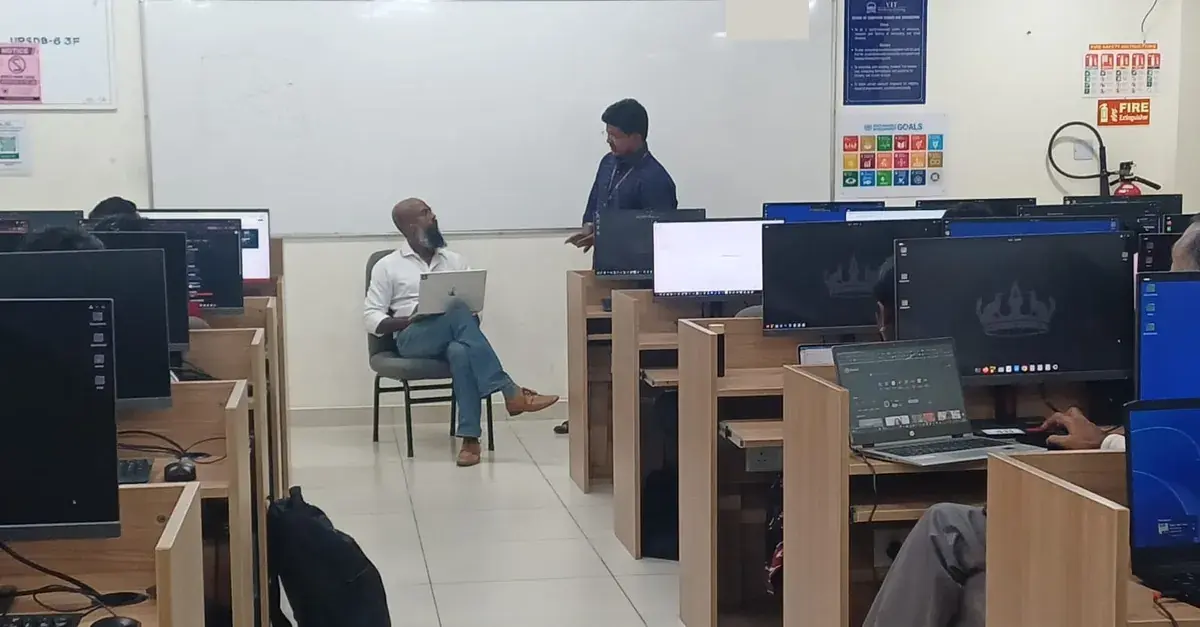 Moses seated with a laptop while a faculty participant discusses work with him